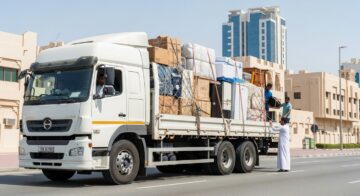 A stressed couple surrounded by cardboard boxes while talking to a mover in Dubai, illustrating the risks of hiring cheap movers in dubai and hidden costs during relocation.